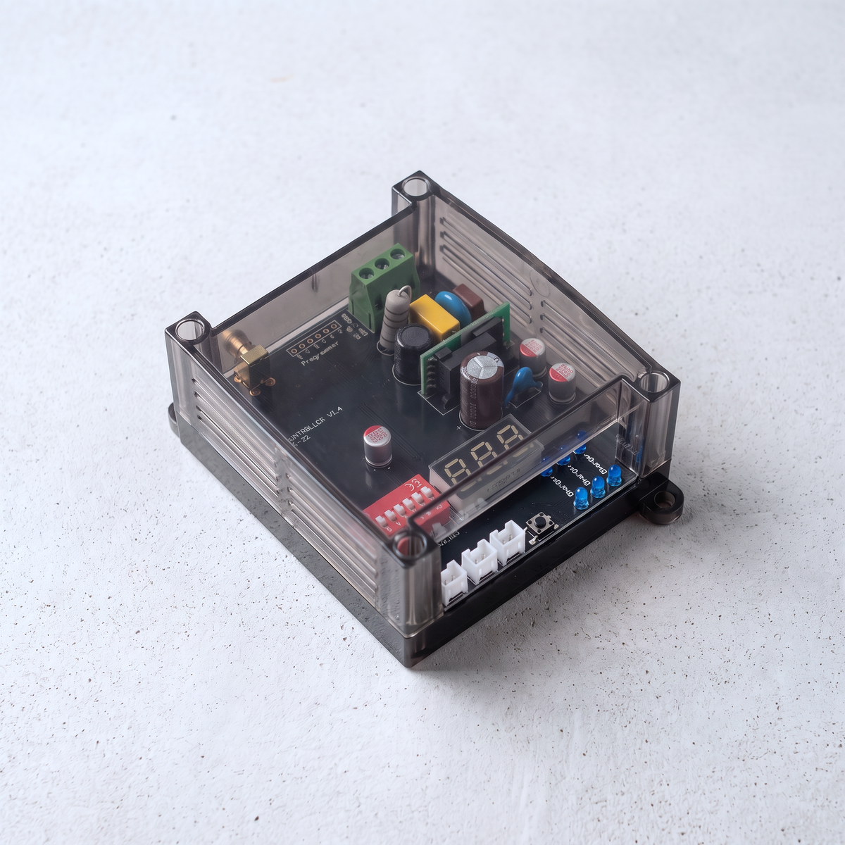 Angled top view of the DLB module in its smoked transparent enclosure resting on a light concrete surface